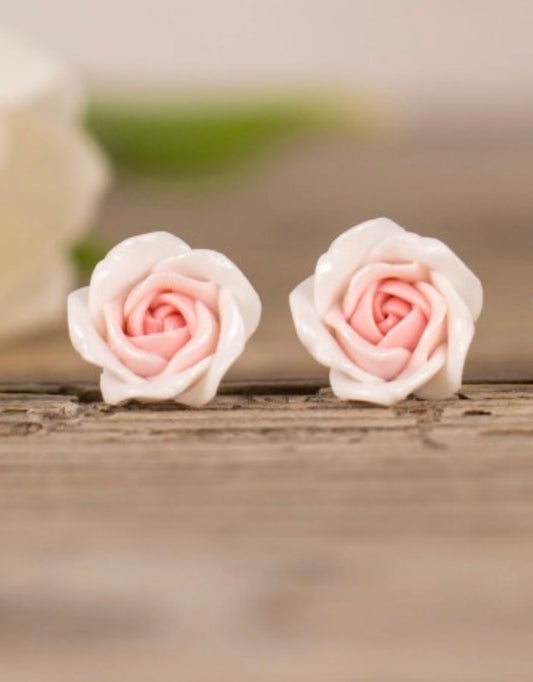 Pair of pink rose-shaped earrings on a wooden surface with a blurred background