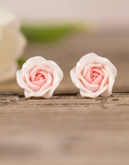 Pair of pink rose-shaped earrings on a wooden surface with a blurred background