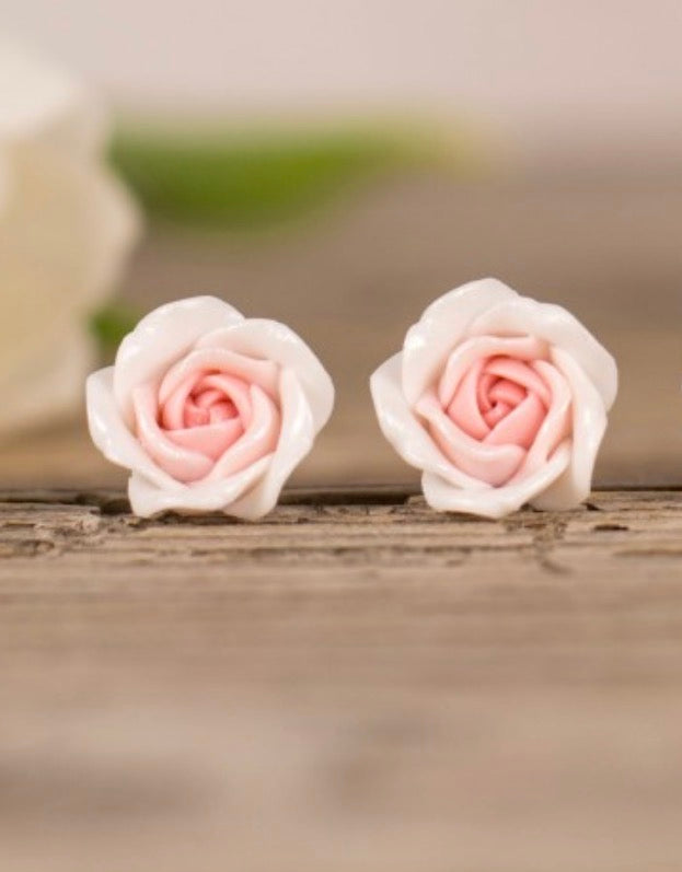 Pair of pink rose-shaped earrings on a wooden surface with a blurred background